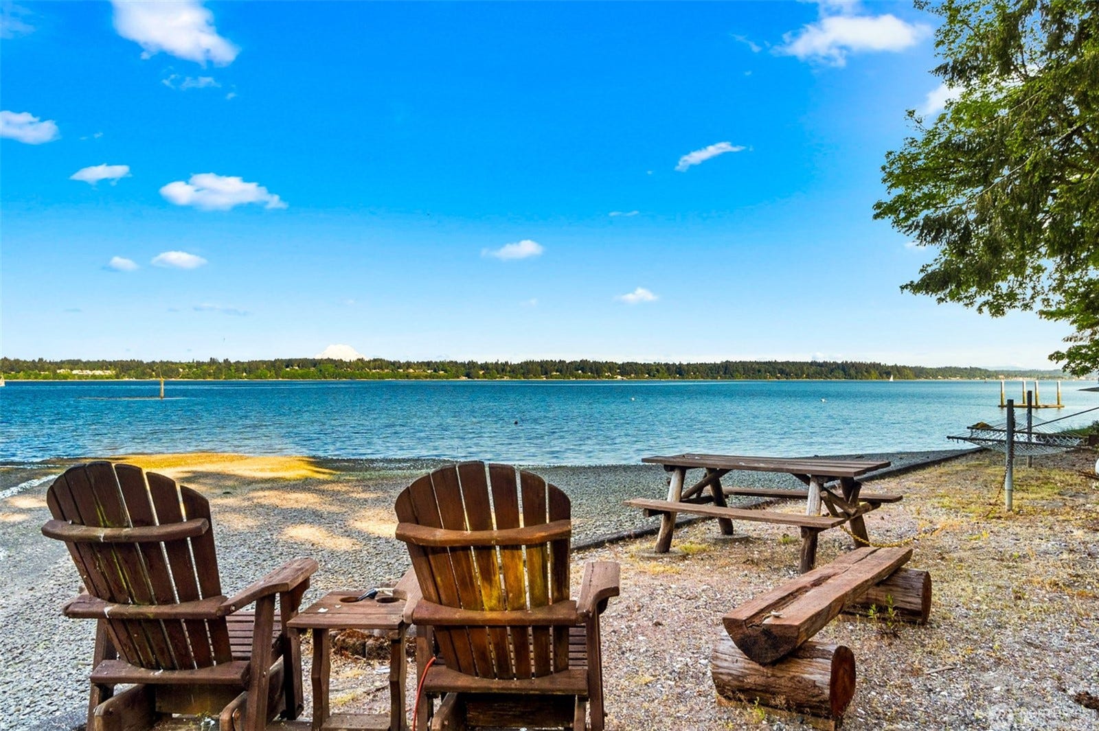 Two Adirondack chairs on a Thurston County waterfront beach looking across the water toward the tree line.